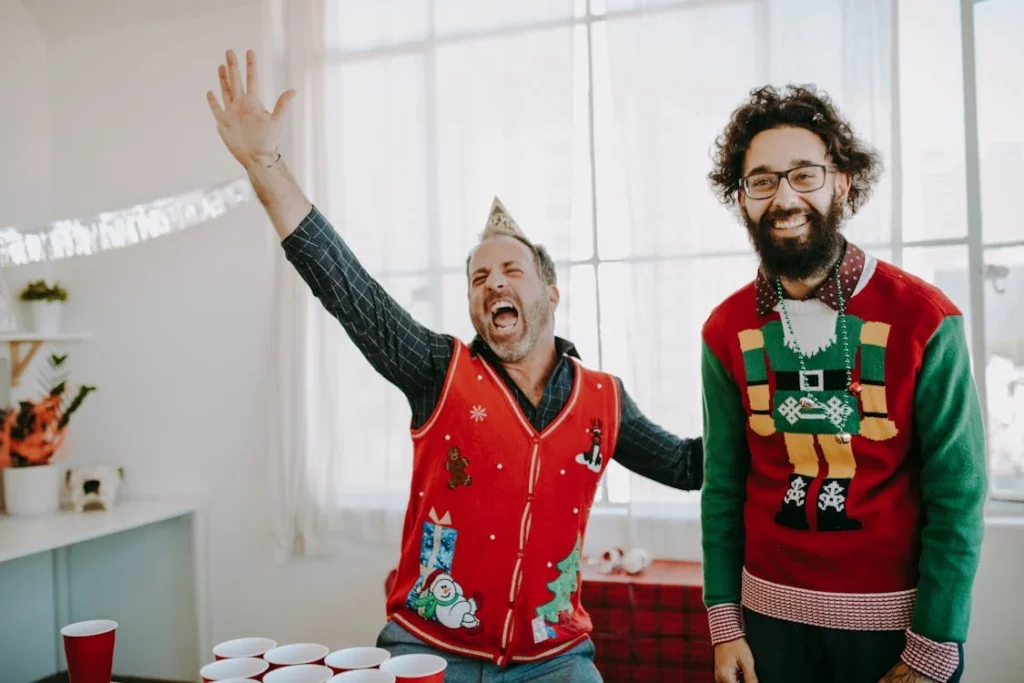 Two fellows in ugly holiday sweaters smile and celebrate a fun holiday party